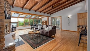 A spacious living room with a wooden ceiling, a fireplace, a sofa, and a dining area with a table and chairs.