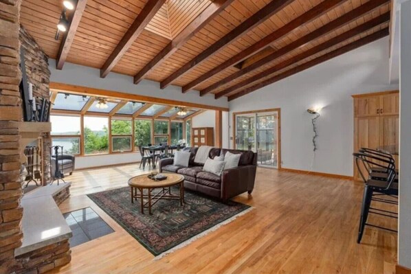 Un vaste salon doté d’un plafond en bois, d’une cheminée, d’un canapé et d’un coin repas avec une table et des chaises.
