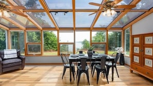 A dining area with a table set for six, surrounded by chairs, under a glass ceiling with a ceiling fan.