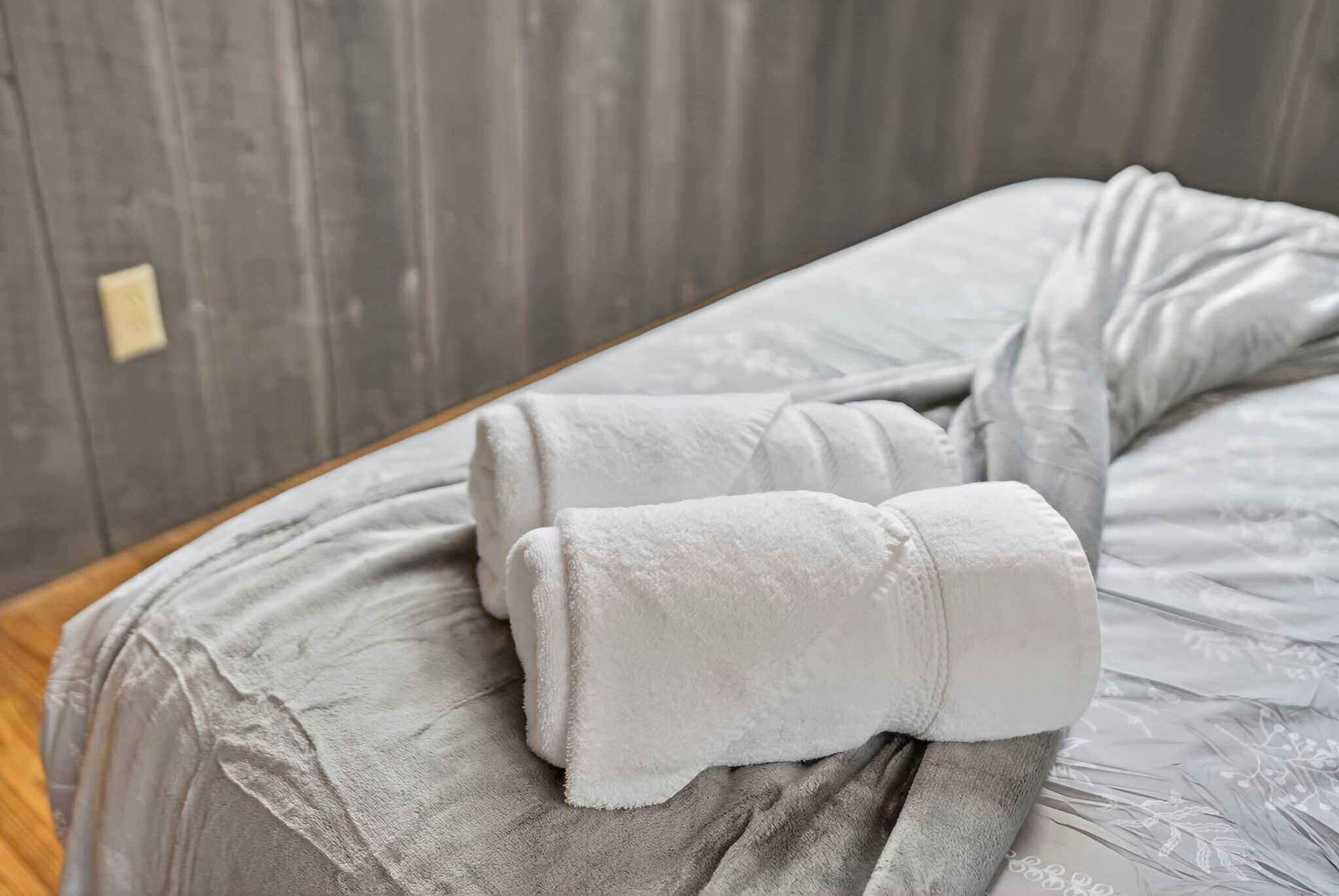 A neatly made bed with a grey blanket and a rolled-up towel on the side.