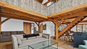 Een ruime loft met zichtbare houten balken, een glazen salontafel, een bank en een trap.