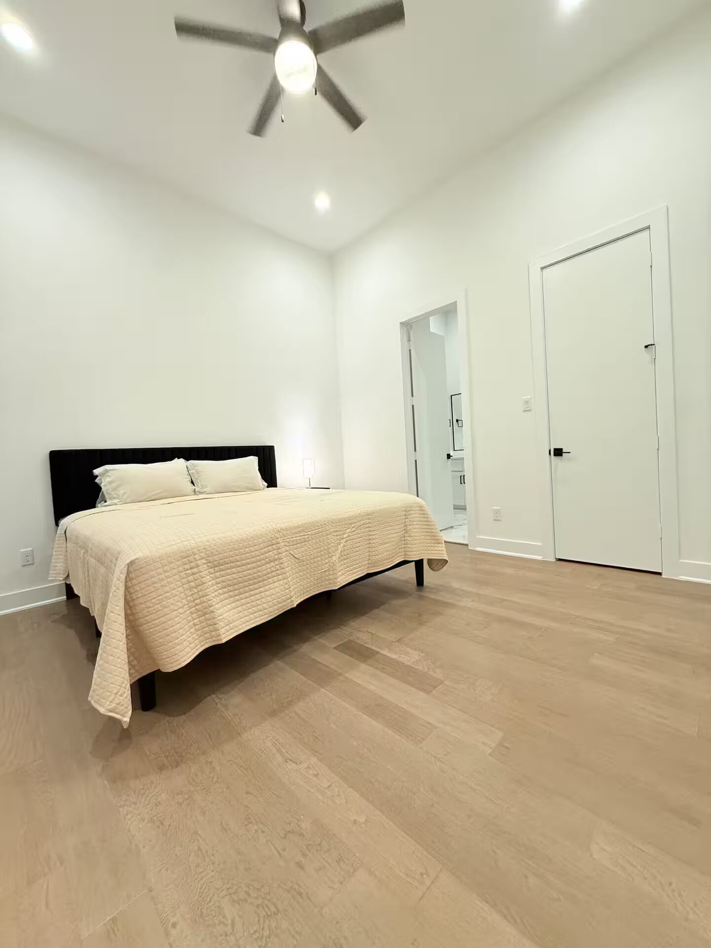 A bedroom with a bed, a ceiling fan, and a door.