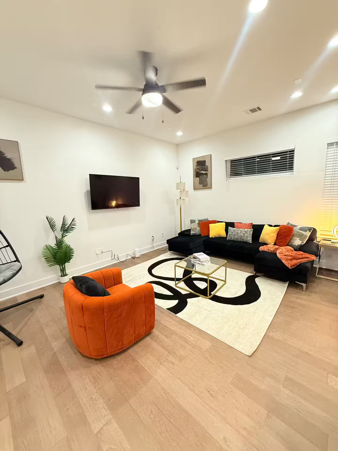Ein modernes Wohnzimmer mit einer schwarzen Couch, einem orangefarbenen Sessel und einem Couchtisch.