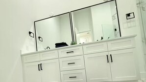 A modern bathroom with a white vanity, a large mirror, and a black rug on a marble floor. - 3-bedroom house in serene Houston with cool AC for relaxing stays (Houston)