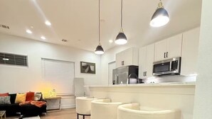 A modern kitchen with white cabinets, a stainless steel microwave, and a bar area with three white barstools. - 3-bedroom house in serene Houston with cool AC for relaxing stays (Houston)