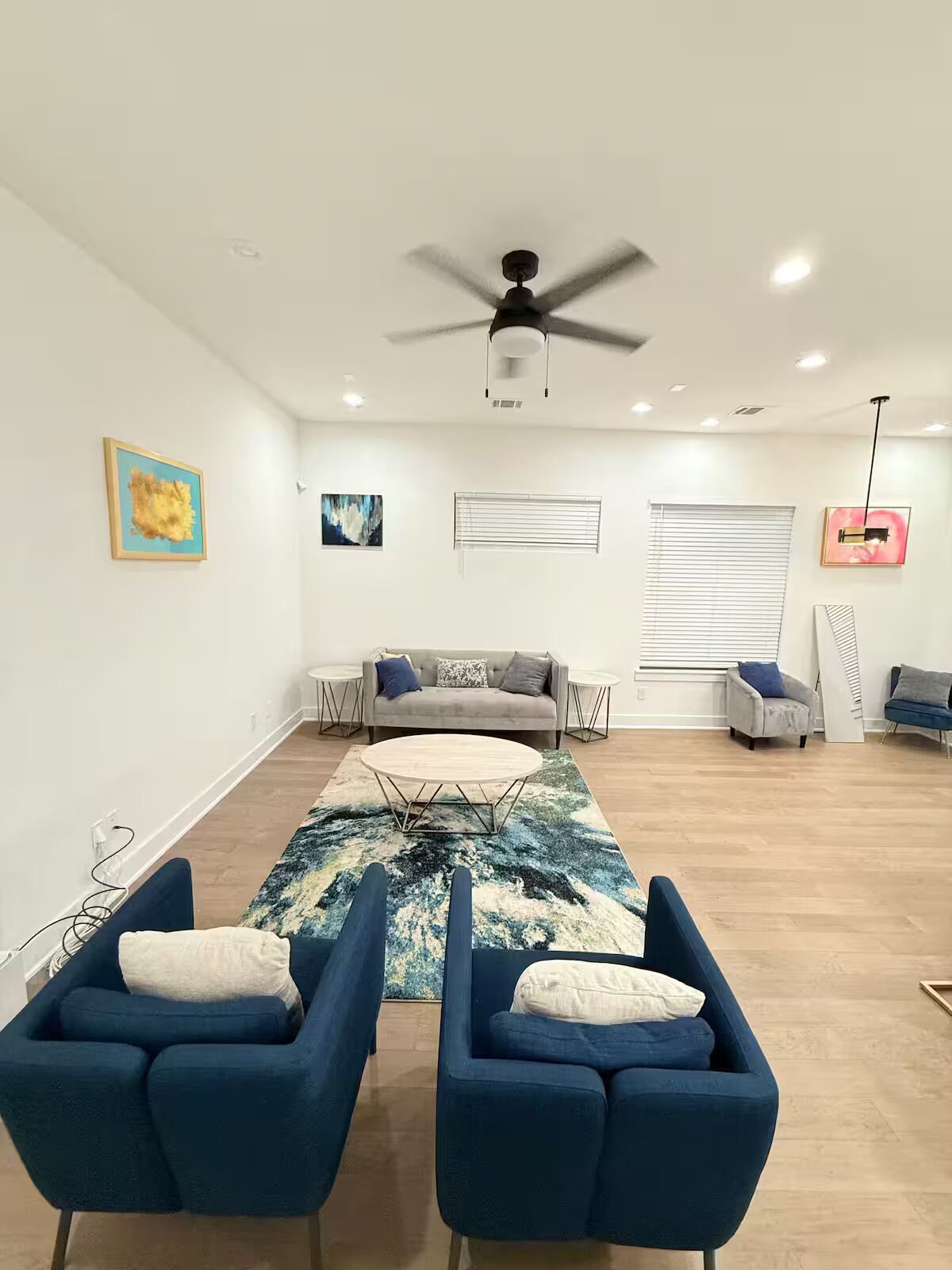 Ein geräumiges Wohnzimmer mit Deckenventilator, einem grauen Sofa, einem Couchtisch und zwei blauen Sesseln.