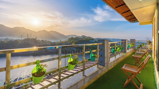 A balcony with a view of a river and mountains, potted plants, and wooden lounge chairs. - Lake Mount (Bhimtal)