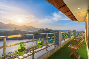 A balcony with a view of a river and mountains, potted plants, and wooden lounge chairs. - Lake Mount (Bhimtal)
