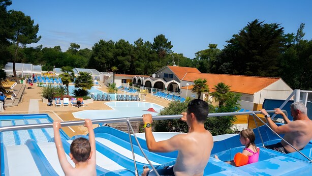 Un tobogán de agua con múltiples carriles, una zona de piscina y un edificio con techo de tejas rojas.