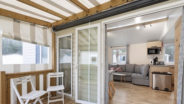 Ein überdachter Außenbereich mit Holzterrasse, einer Schiebetür zu einem Wohnzimmer und einer kleinen Küchenzeile.
