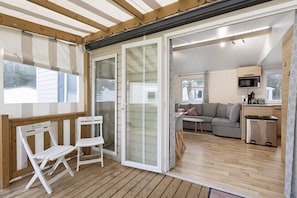 A covered outdoor area with a wooden deck, a sliding glass door leading to a living room, and a small kitchen area.