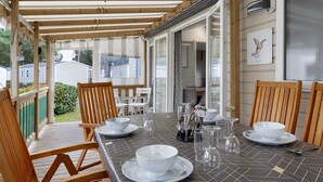 Ein überdachter Essbereich im Freien mit Holzbänken und einem Tisch für vier Personen, mit Fliesenboden und Blick in den Garten.