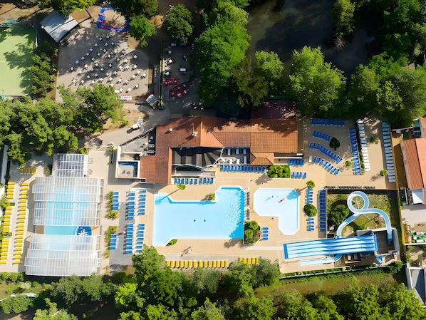 An aerial view of a resort with a swimming pool, sun loungers, a water slide, and a parking area.