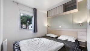 Ein Schlafzimmer mit Bett, Fenster mit Vorhängen, einer Wandablage und einer Nachttischlampe.