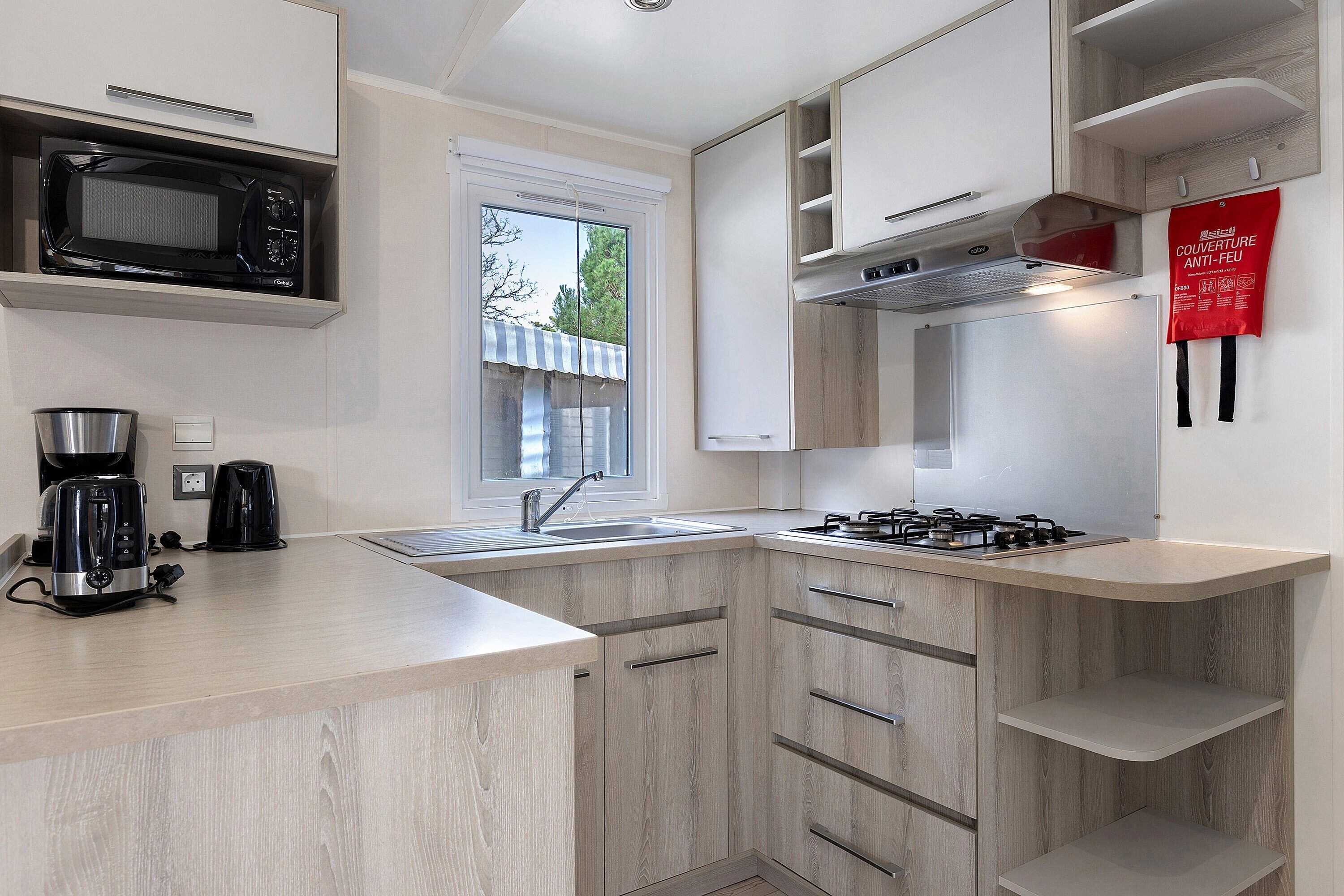 Een moderne keuken met een magnetron, broodrooster, spoelbak, fornuis en houten kastjes.