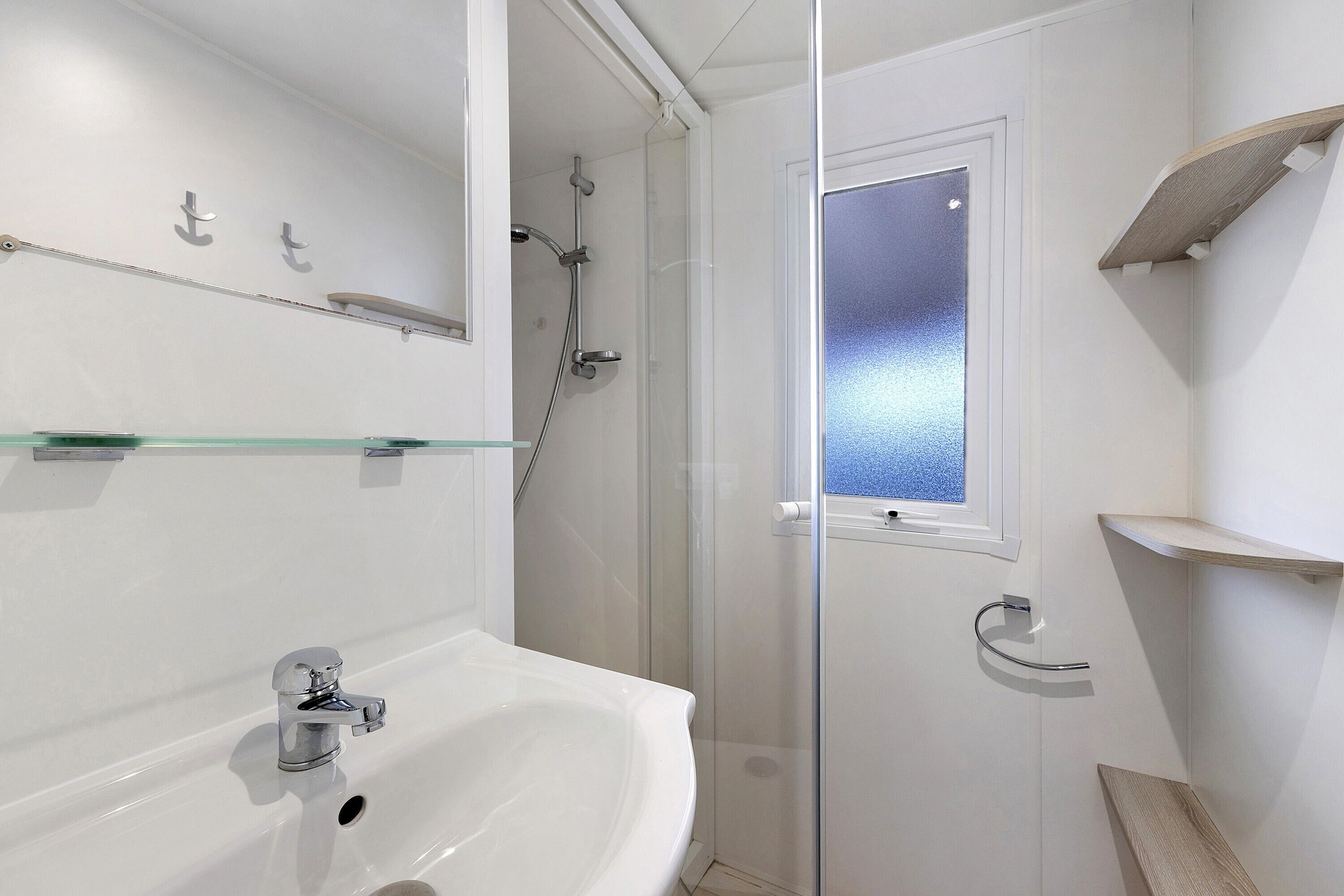 A bathroom with a glass shower enclosure, a white sink, and a window.