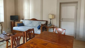 Una habitació amb taula de dinar de fusta, un sofà amb coixinets estampats, una làmpada i un televisor sobre un suport de fusta.