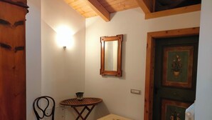 Habitació amb sostre de fusta, un mirall a la paret, una cadira, una taula petita, un armari i una porta amb una pintura floral.
