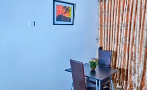 A dining area with a table and chairs, a framed picture on the wall, and a curtain with a floral pattern. - Glitaz Apartment (Abuja)