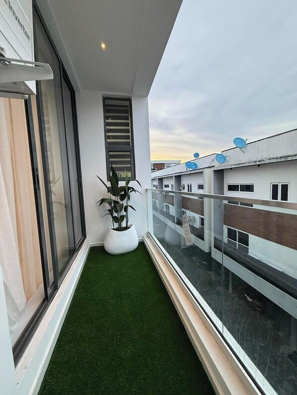 A narrow balcony with artificial grass, a potted plant, and a view of adjacent buildings. - Glitaz Apartment (Abuja)