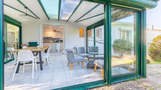 A modern house with a glass-enclosed patio, a dining area, and a kitchen. - Family home in central Fromentine with terrace, Wi-Fi, air conditioning, €800 security deposit (La Barre-de-Monts)