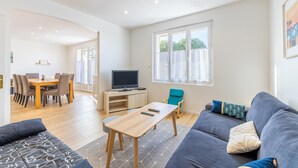 A modern living room with a sofa, a coffee table, a TV, and a dining area with chairs and a table. - Family home in central Fromentine with terrace, Wi-Fi, air conditioning, €800 security deposit (La Barre-de-Monts)
