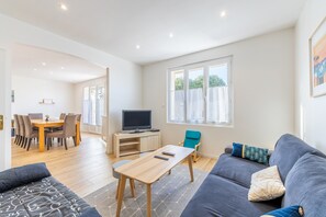 Ett modernt vardagsrum med en soffa, ett soffbord, en tv och en matplats med stolar och ett bord.