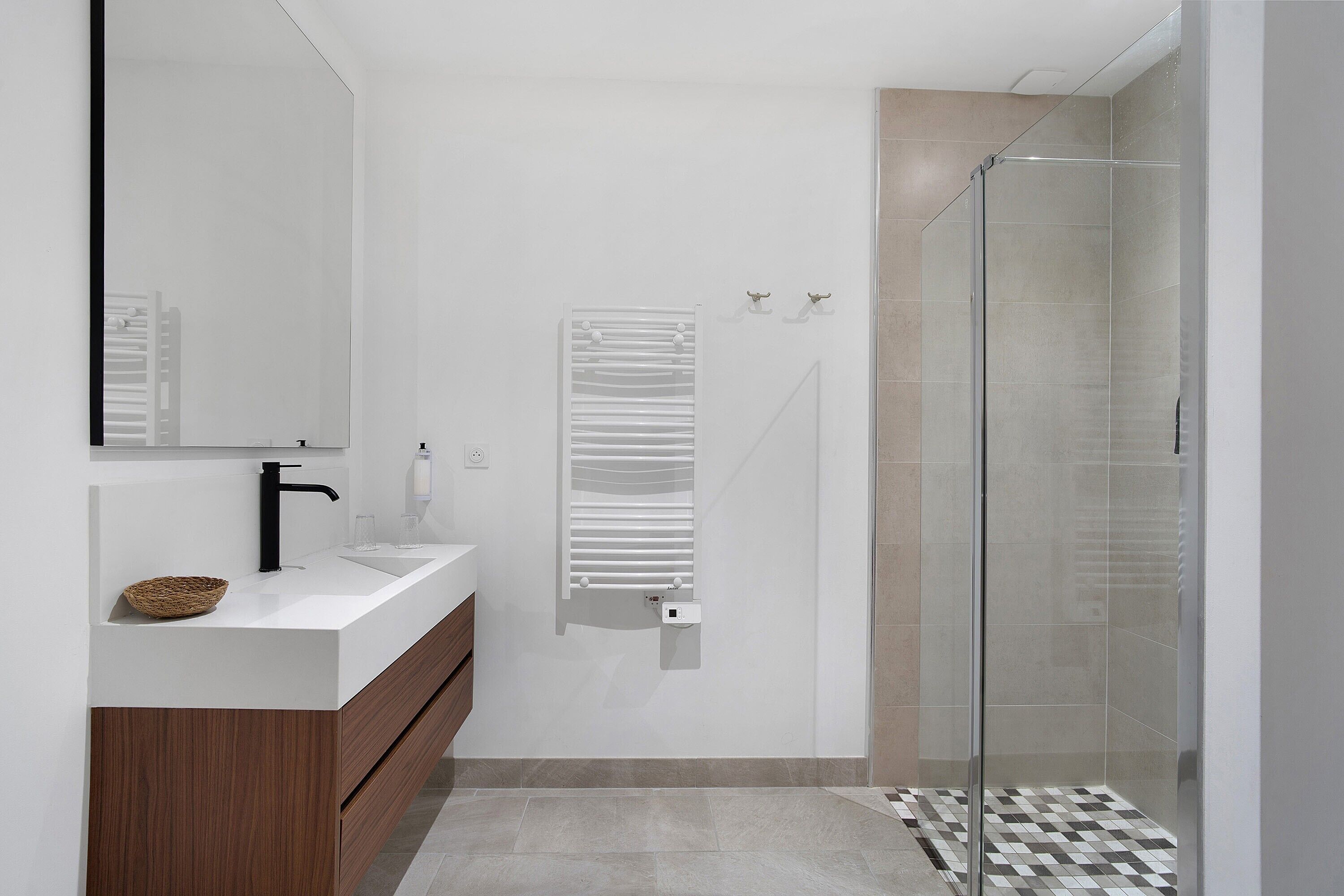 Ein modernes Badezimmer mit einer Duschkabine aus Glas, einem weißen Waschbecken mit schwarzem Wasserhahn und einer Holzausstattung.