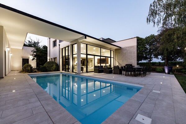 A modern house with a swimming pool, outdoor seating, and a covered patio area.