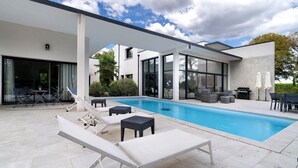 Et moderne poolområde med liggestole, grill og en terrasse med udendørs møbler.