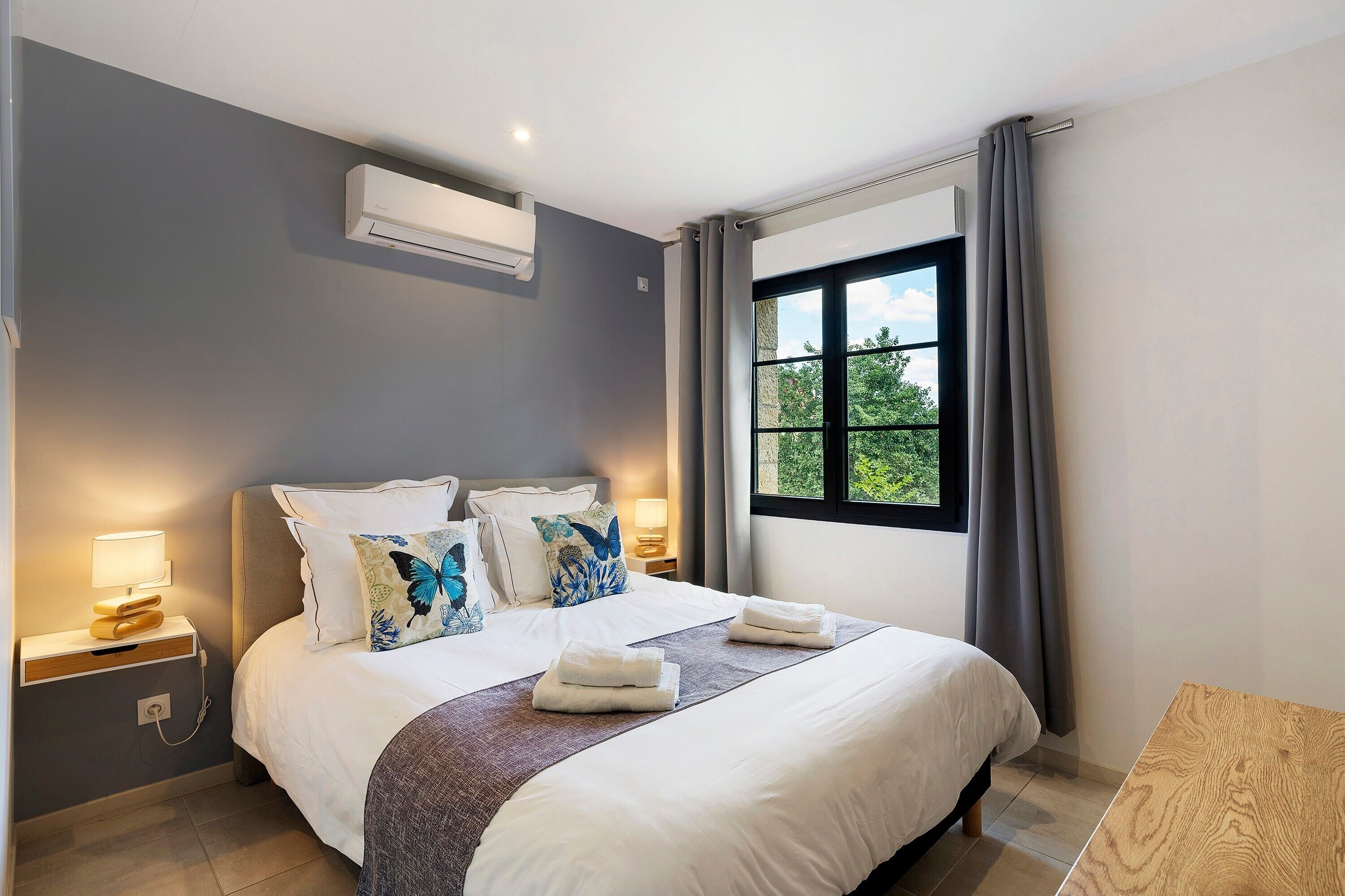 Una habitación de hotel moderna con una cama grande, lámparas de noche, una ventana con cortinas y un equipo de aire acondicionado.