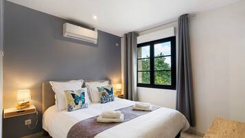 Una habitación de hotel moderna con una cama grande, lámparas de noche, una ventana con cortinas y un equipo de aire acondicionado.