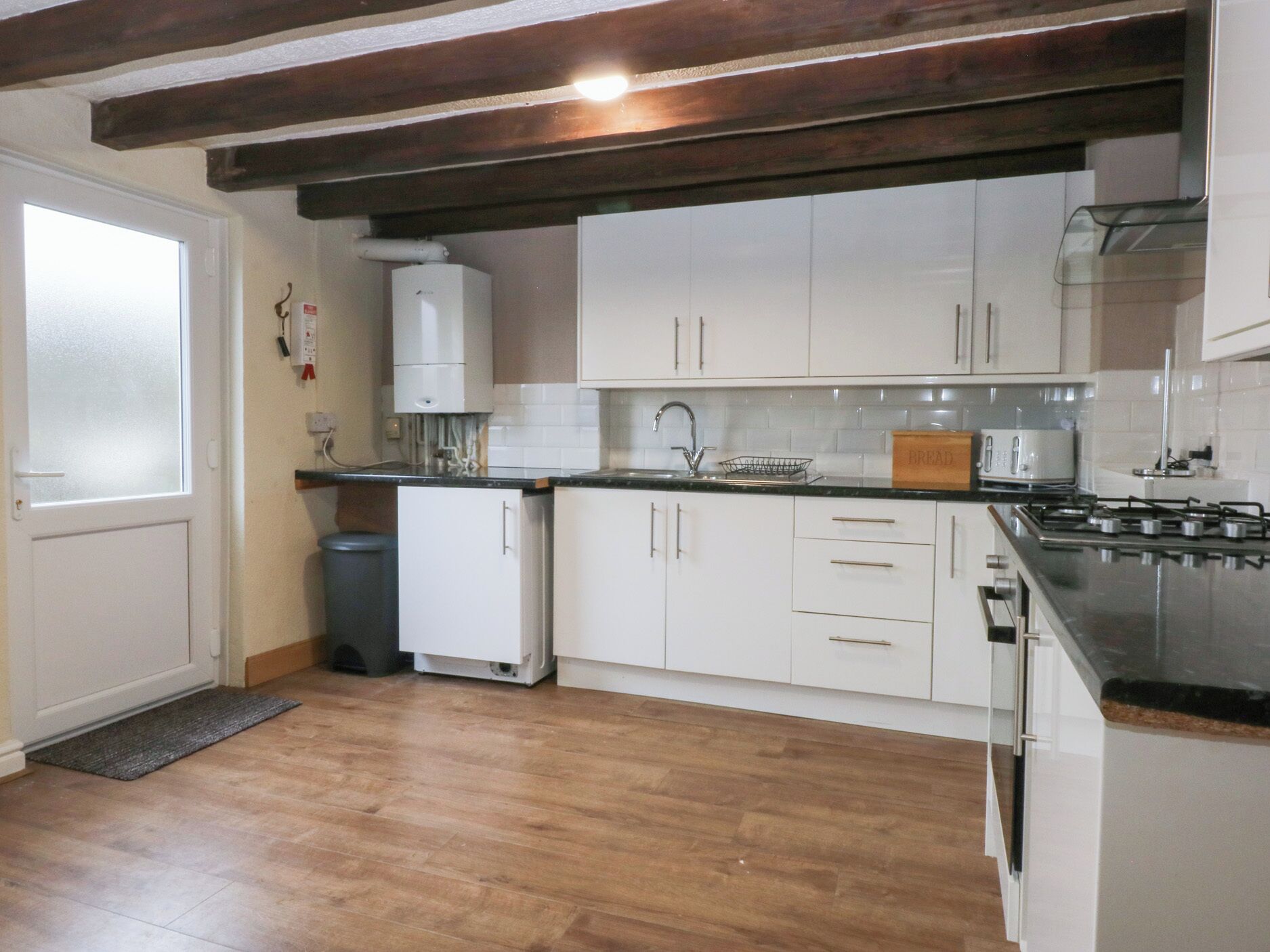 A modern kitchen with white cabinets, a black countertop, and a wooden floor.