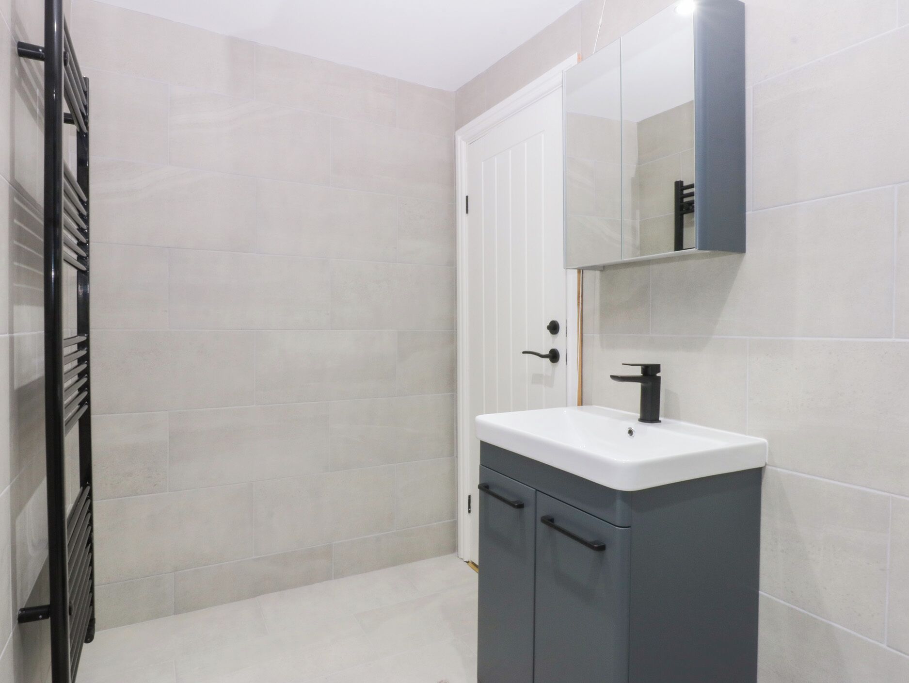 A bathroom with a white tiled wall, a grey cabinet with a white sink, and a black towel rack.