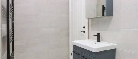 A bathroom with a white tiled wall, a grey cabinet with a white sink, and a black towel rack.