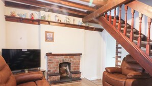 Una sala de estar con chimenea de ladrillo, sofás de cuero, una escalera de madera y un televisor.