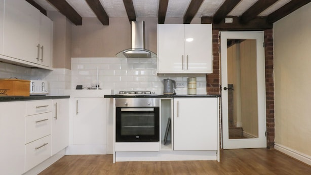 Una cocina compacta con armarios blancos, horno de acero inoxidable y techo de madera.
