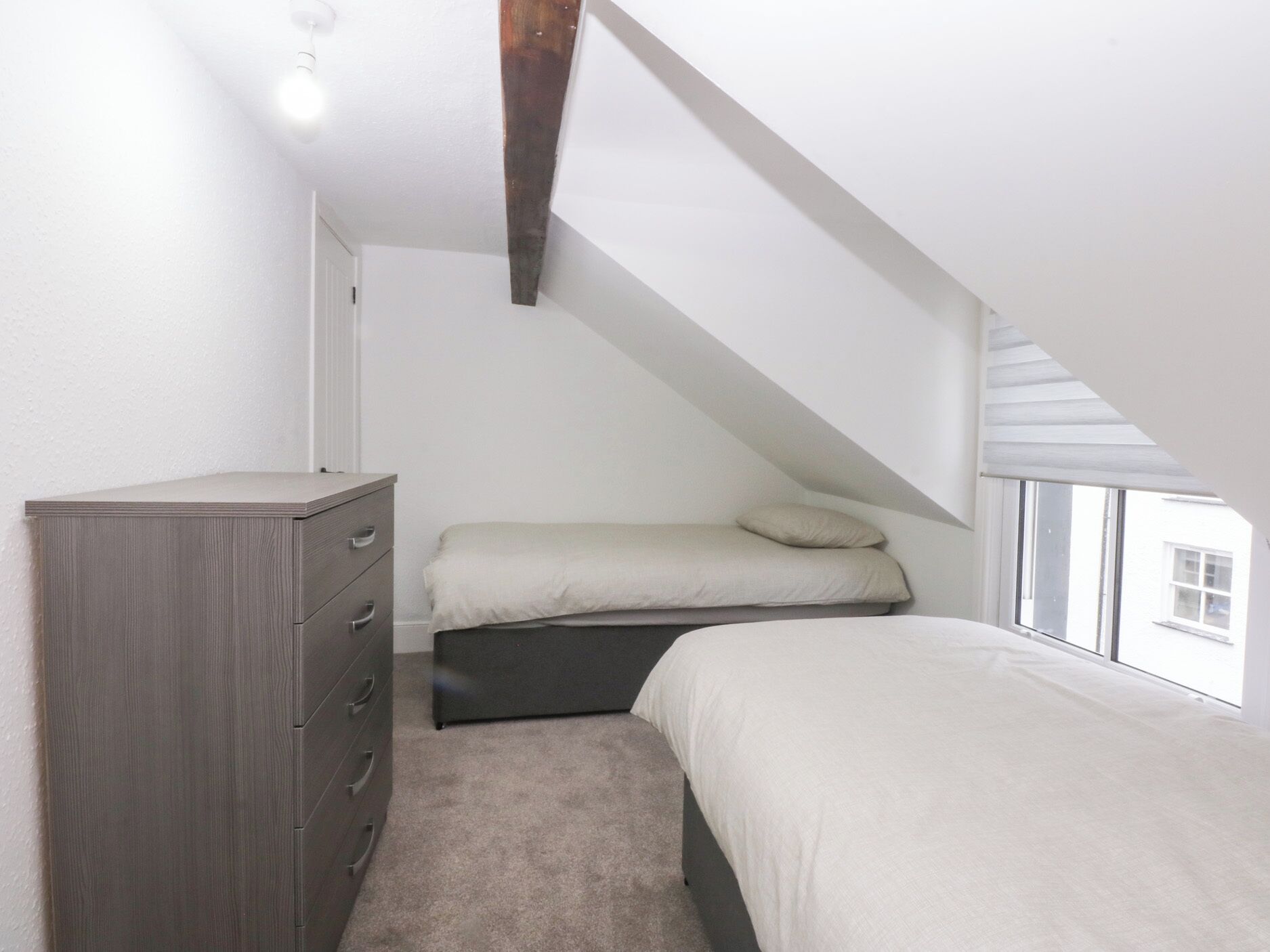 A bedroom with a sloped ceiling, a bed, a dresser, and a window.