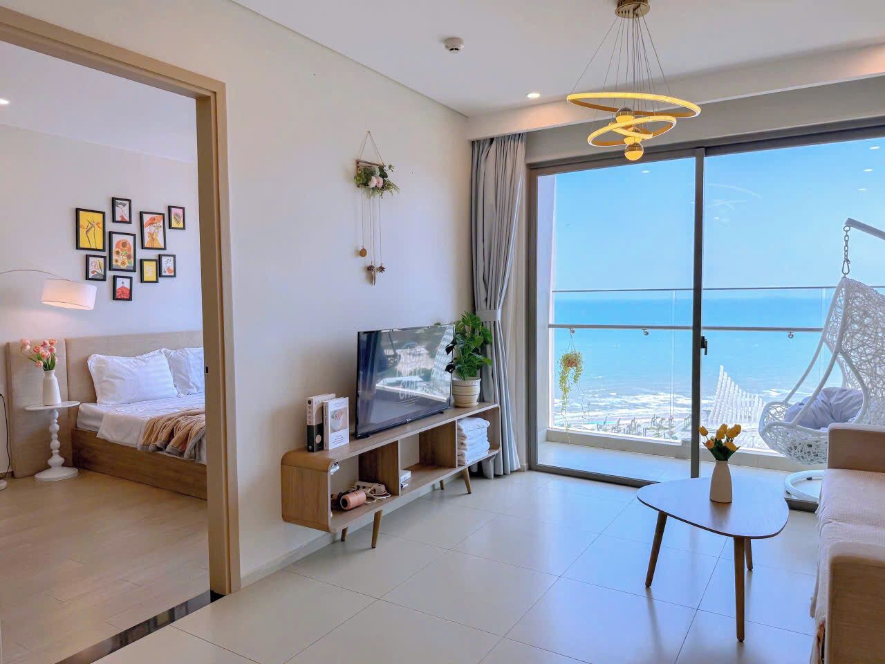A modern hotel room with a bed, TV, seating area, and a balcony with a view of the sea.