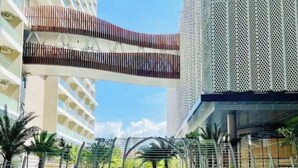 A modern building with a covered walkway, palm trees, and a clear sky. - THE SÓNG Apartment Vũng Tàu - ViVi Home (Ho Chi Minh City)