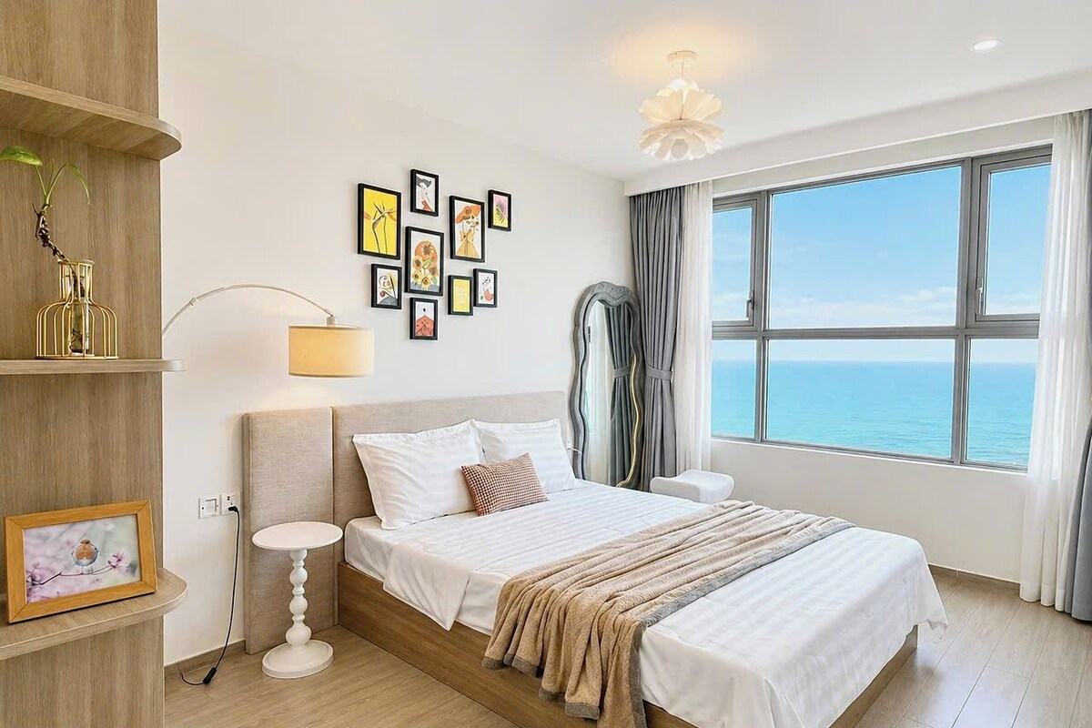Un dormitorio con cama, mesita de noche, lámpara, decoración en la pared y un ventanal con vistas.