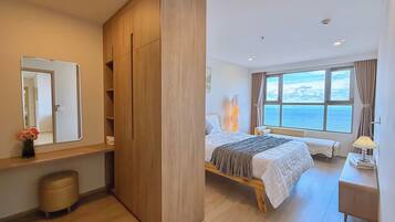 A modern bedroom with a large wardrobe, a bed with a view of the sea, a bedside table with a lamp, and a small stool.