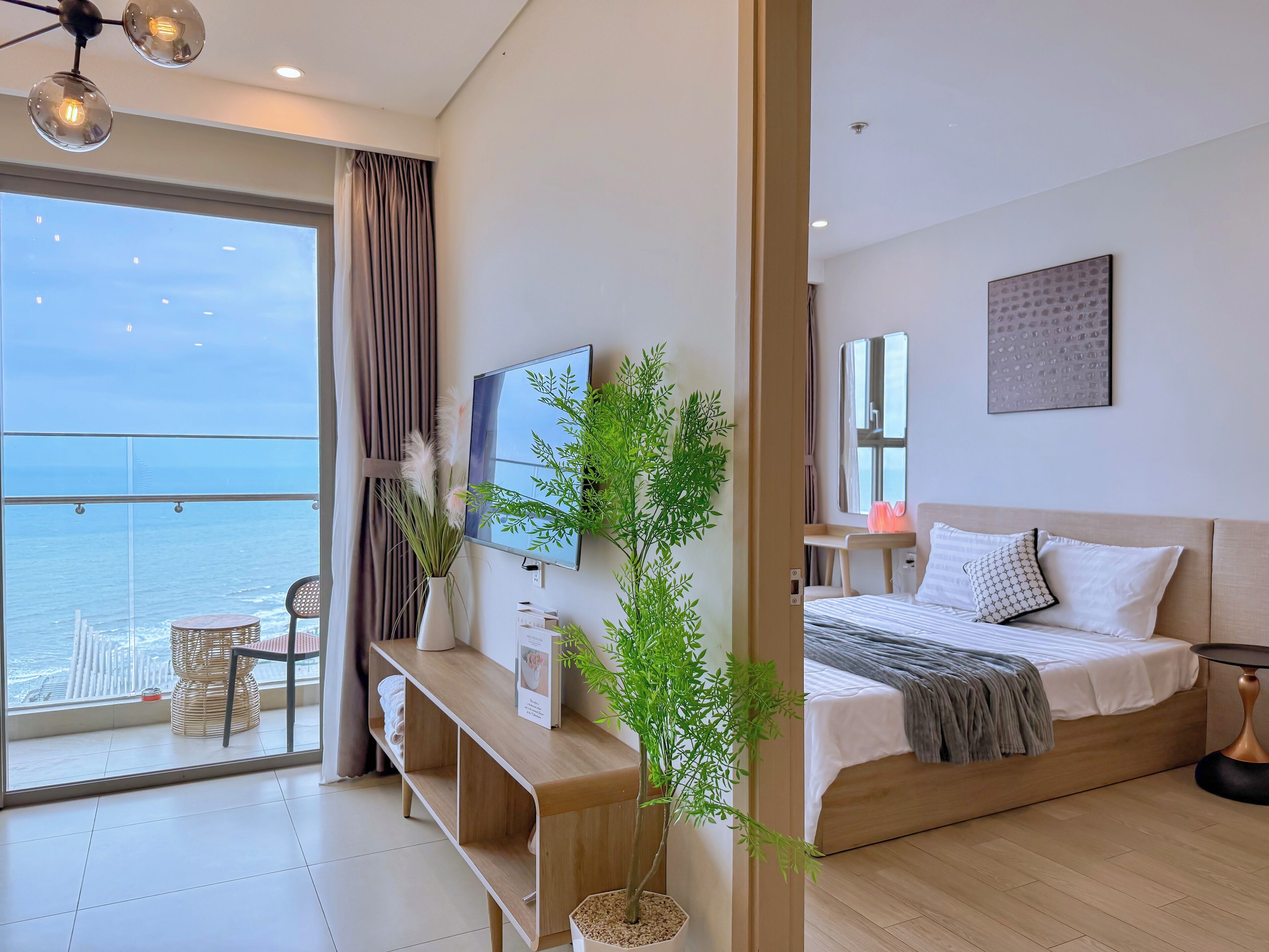 A modern hotel room with a balcony, a bed, a TV, and a potted plant.