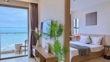 A modern hotel room with a balcony, a bed, a TV, and a potted plant.