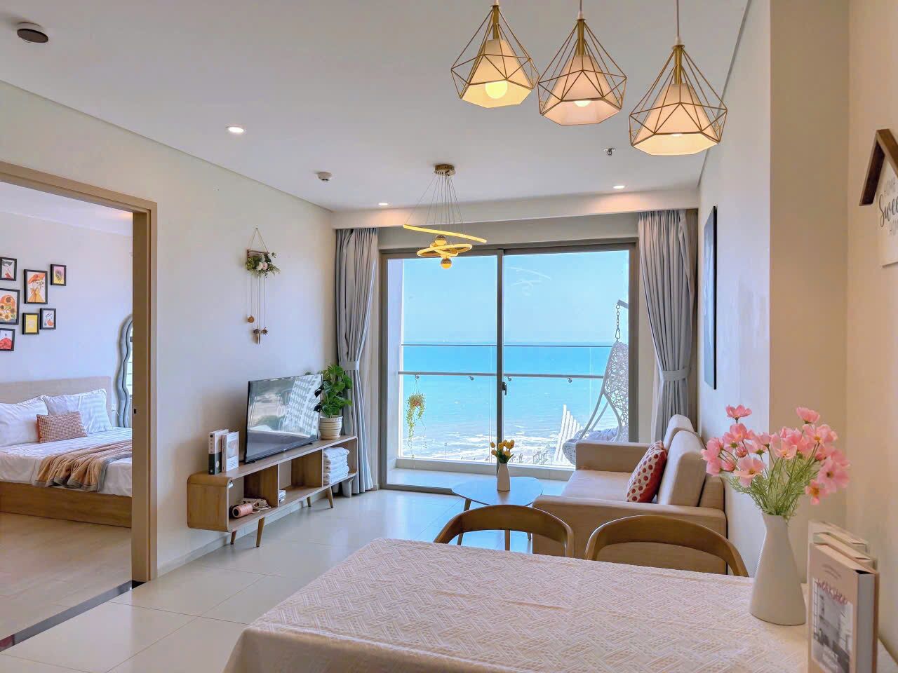 A modern hotel room with a bed, a TV, a dining area, and a balcony with a view of the sea.