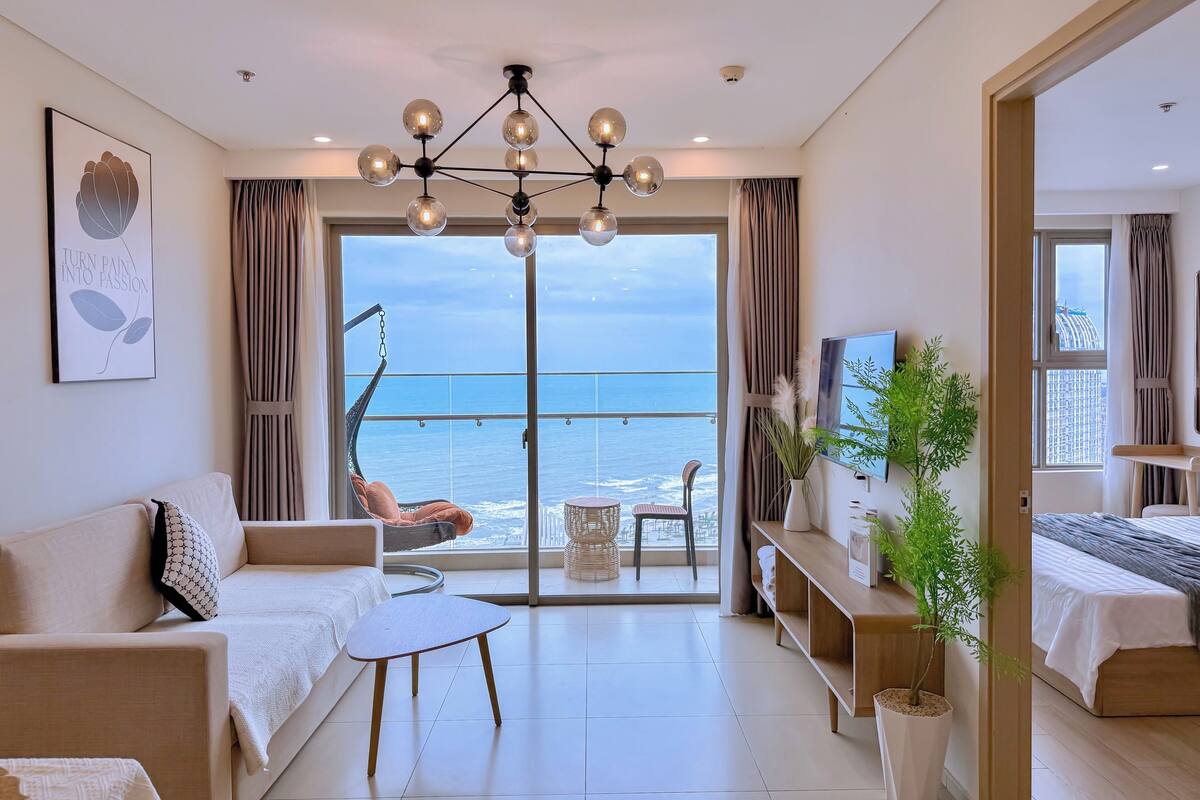 Un salon moderne avec un balcon donnant sur la mer, un fauteuil suspendu, un canapé, une petite table et un téléviseur.