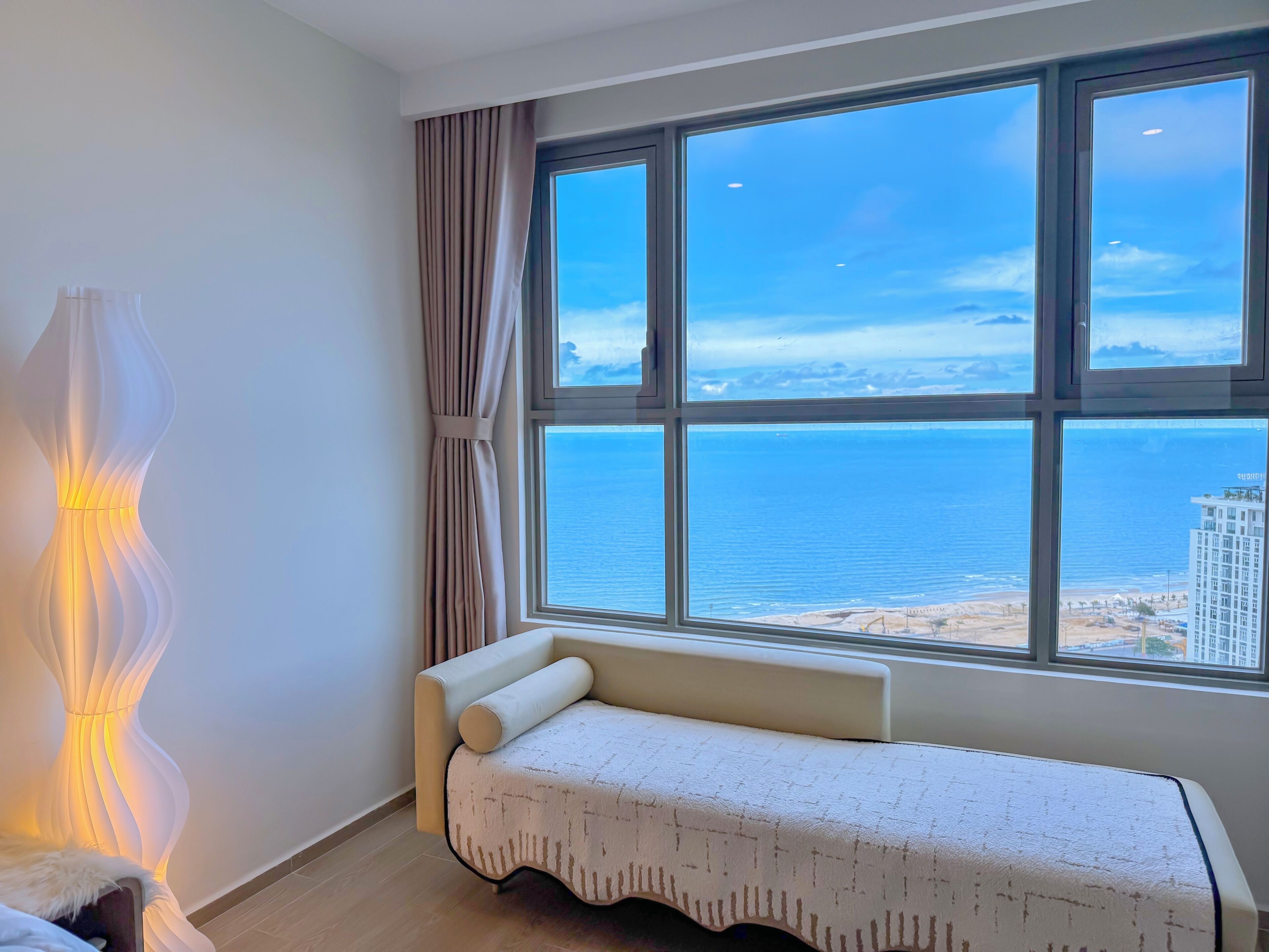 Quarto com uma grande janela que oferece vista para o mar e um edifício do outro lado da água.