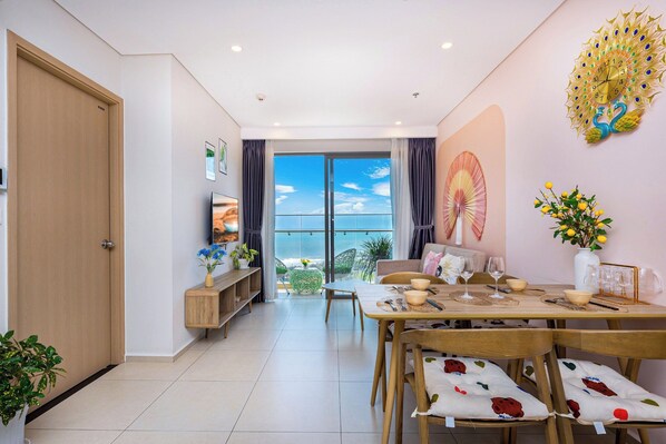 Un comedor con una mesa dispuesta para cuatro personas, vista al océano a través de grandes ventanales y un reloj de pared decorativo.