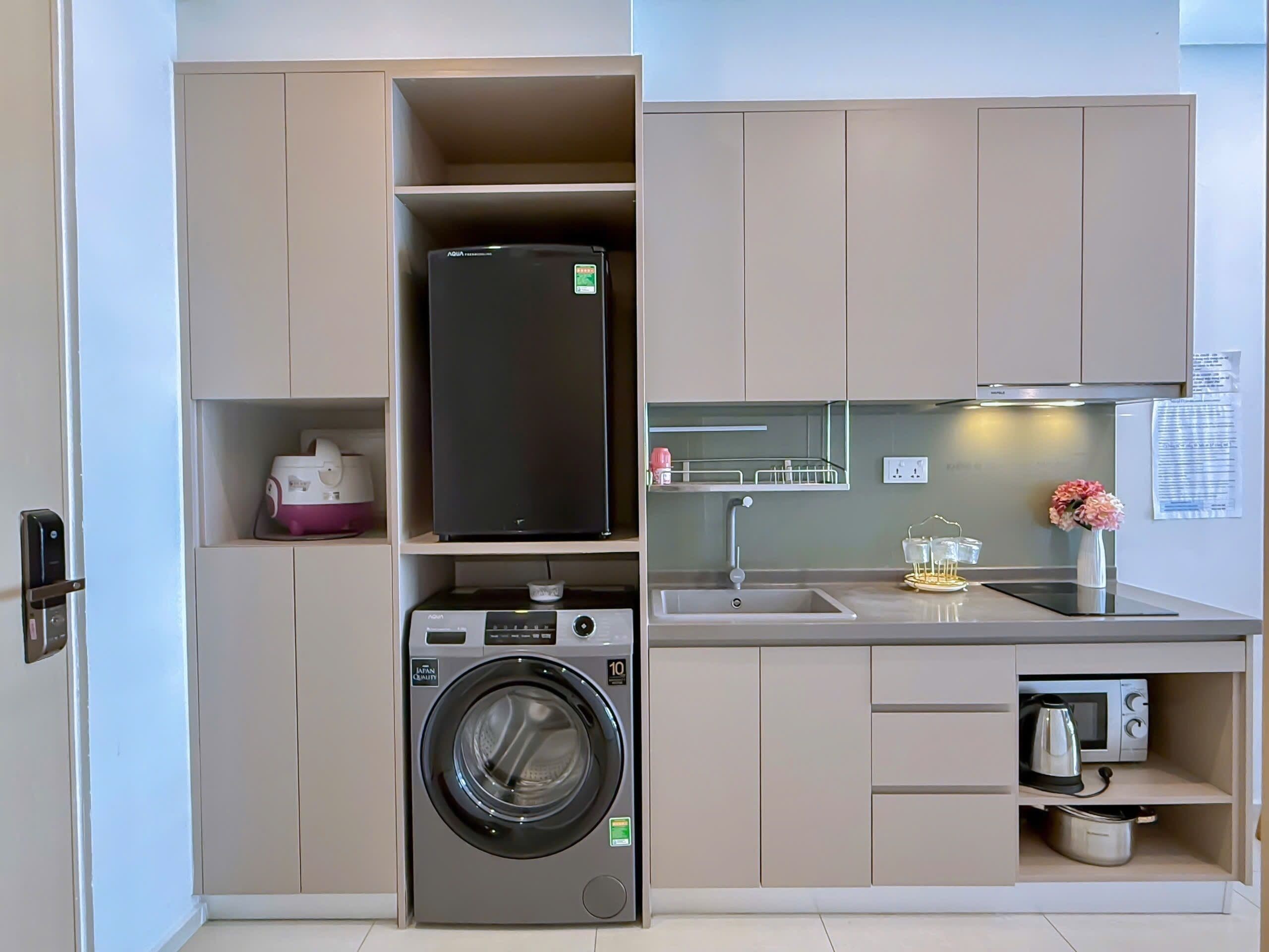 Una cocina compacta con lavadora, refrigerador, microondas y pileta.