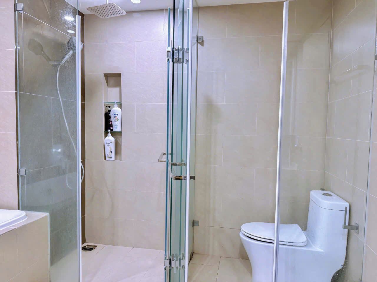 Une salle de bain avec une douche à parois de verre, des toilettes et une étagère contenant des articles de toilette.